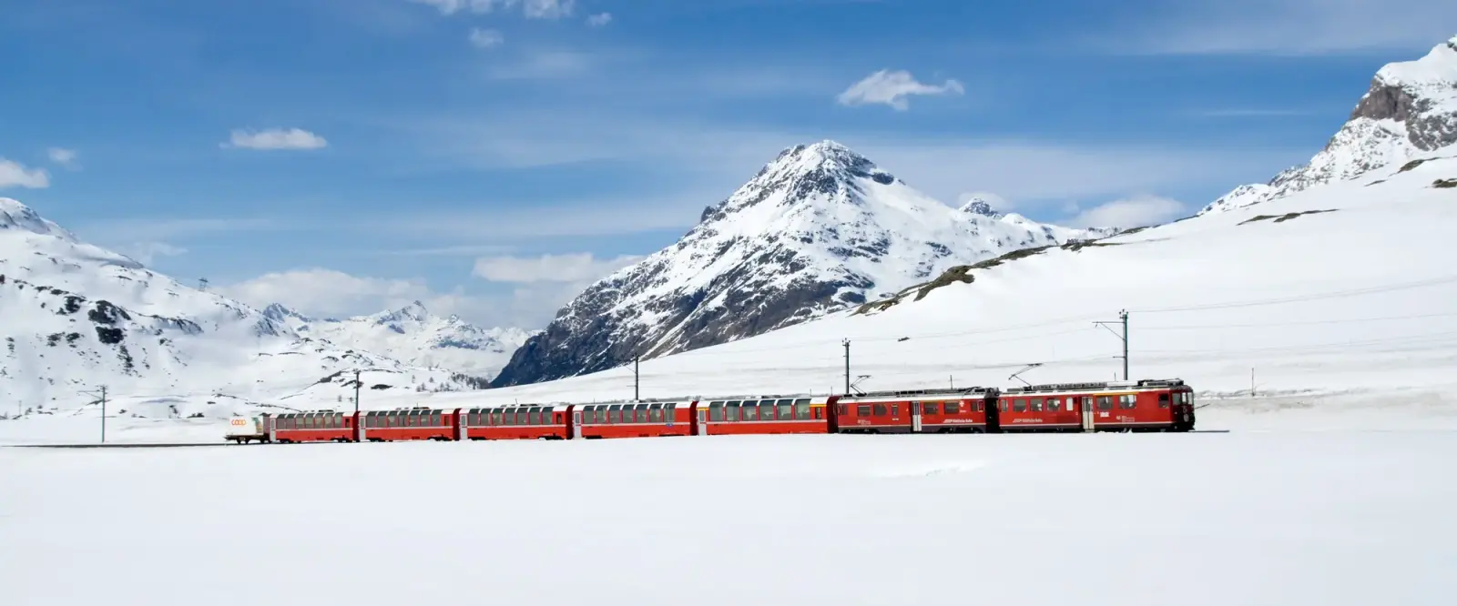 Rode trein van de Berninabahn langs een bevroren meer in een besneeuwd berglandschap