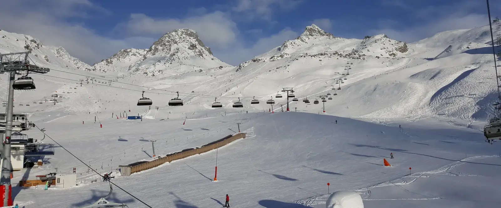 Stoeltjesliften en geprepareerde pistes in een besneeuwde bergkom onder een blauwe lucht